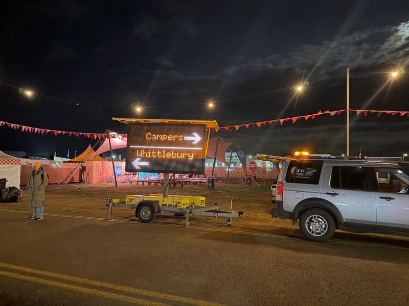 Illuminated sign directing campers at a festival entrance at night