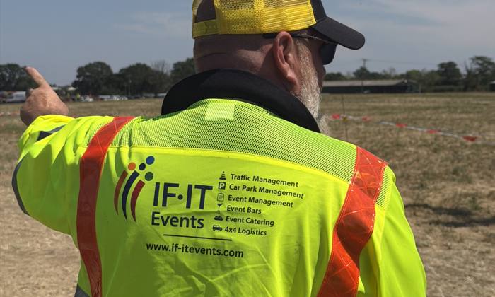IF-IT Events marshal in a hi-vis jacket directing cars in a field